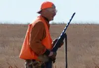 Hunter in orange vest holding a rifle in a field.