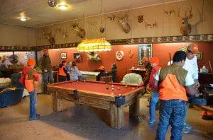 People enjoying a game of pool in a cozy, rustic room with hunting decor.